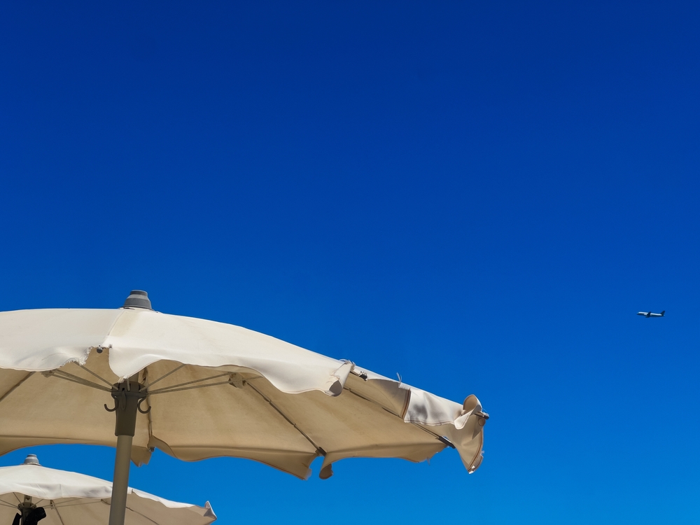 White beach umbrellas against a clear blue sky  symbolizing the risks of a flying umbrella injury at the Jersey Shore.