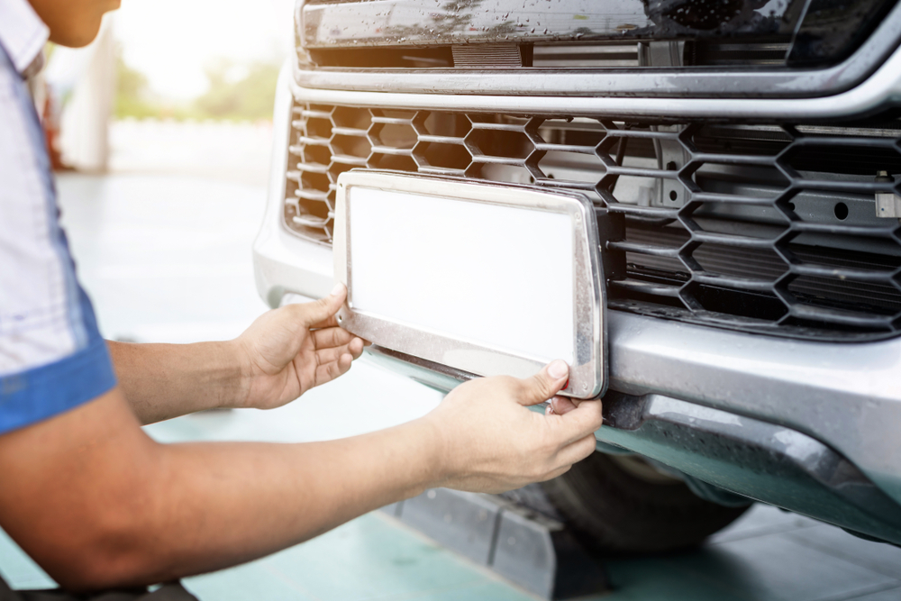 Person attaching temporary license plates to the front of a car, representing the risks of a temporary plates accident with no insurance coverage.