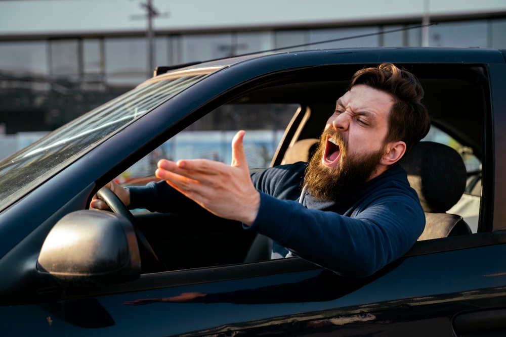 Angry driver yelling and gesturing out of his car window, illustrating the dangers of a road rage incident in New Jersey.