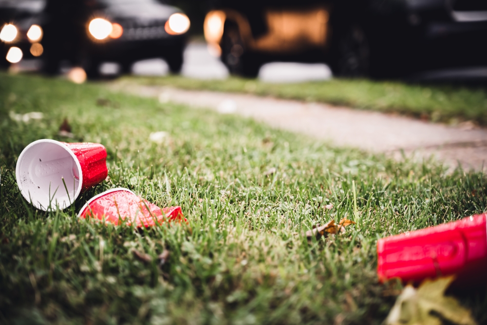 Discarded red plastic cups on grass with cars in the background, representing college parties and hazing risks in New Jersey.