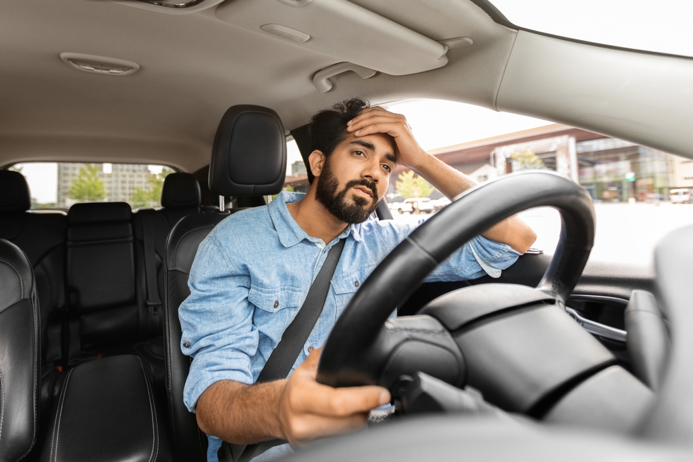 Tired driver resting his hand on his forehead while sitting behind the wheel, illustrating fatigue risk during overnight Thanksgiving travel in New Jersey.