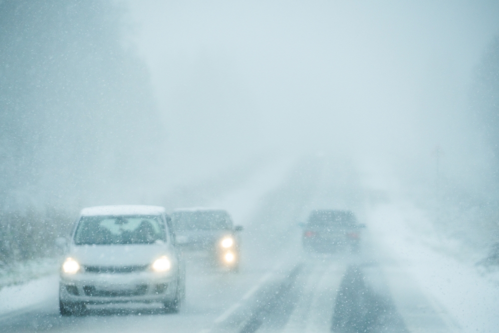 Commuters driving through heavy snow and low visibility on a highway, illustrating the high risk of winter car accidents during the New Jersey holiday season.