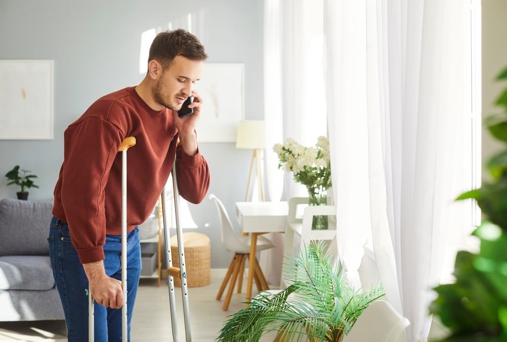 Injured man on crutches using a mobile phone to discuss personal injury claims with a lawyer.