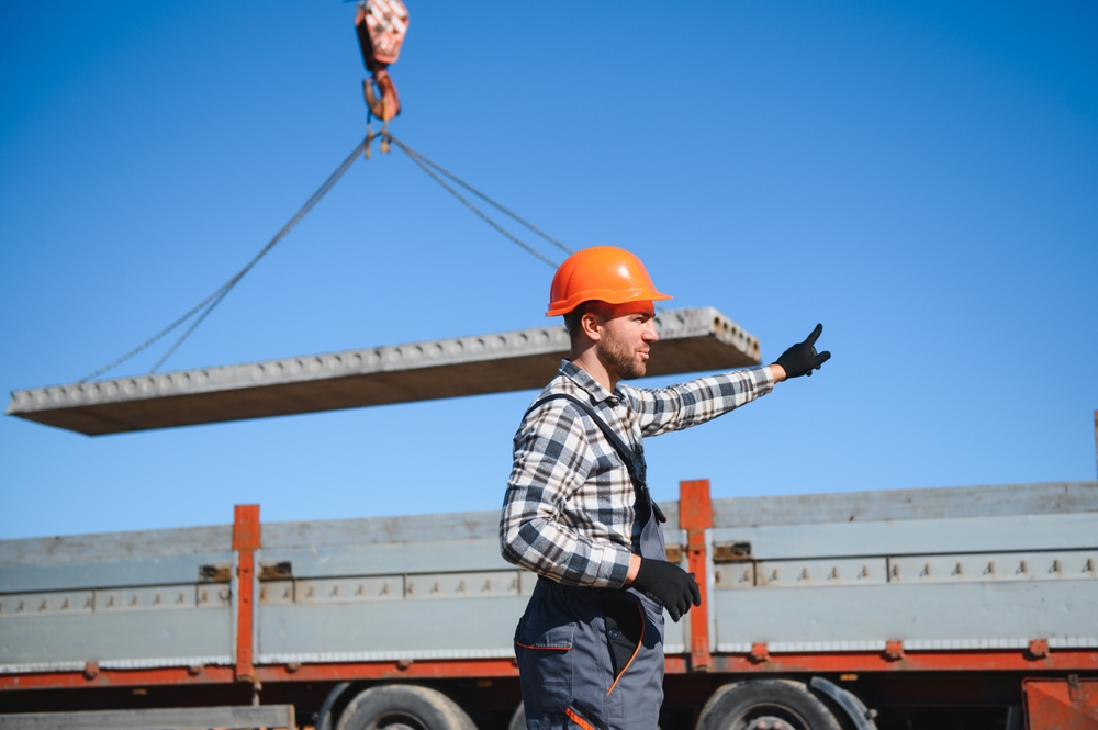 Construction worker directing crane operation on busy job site, representing spring construction accident risks and injuries