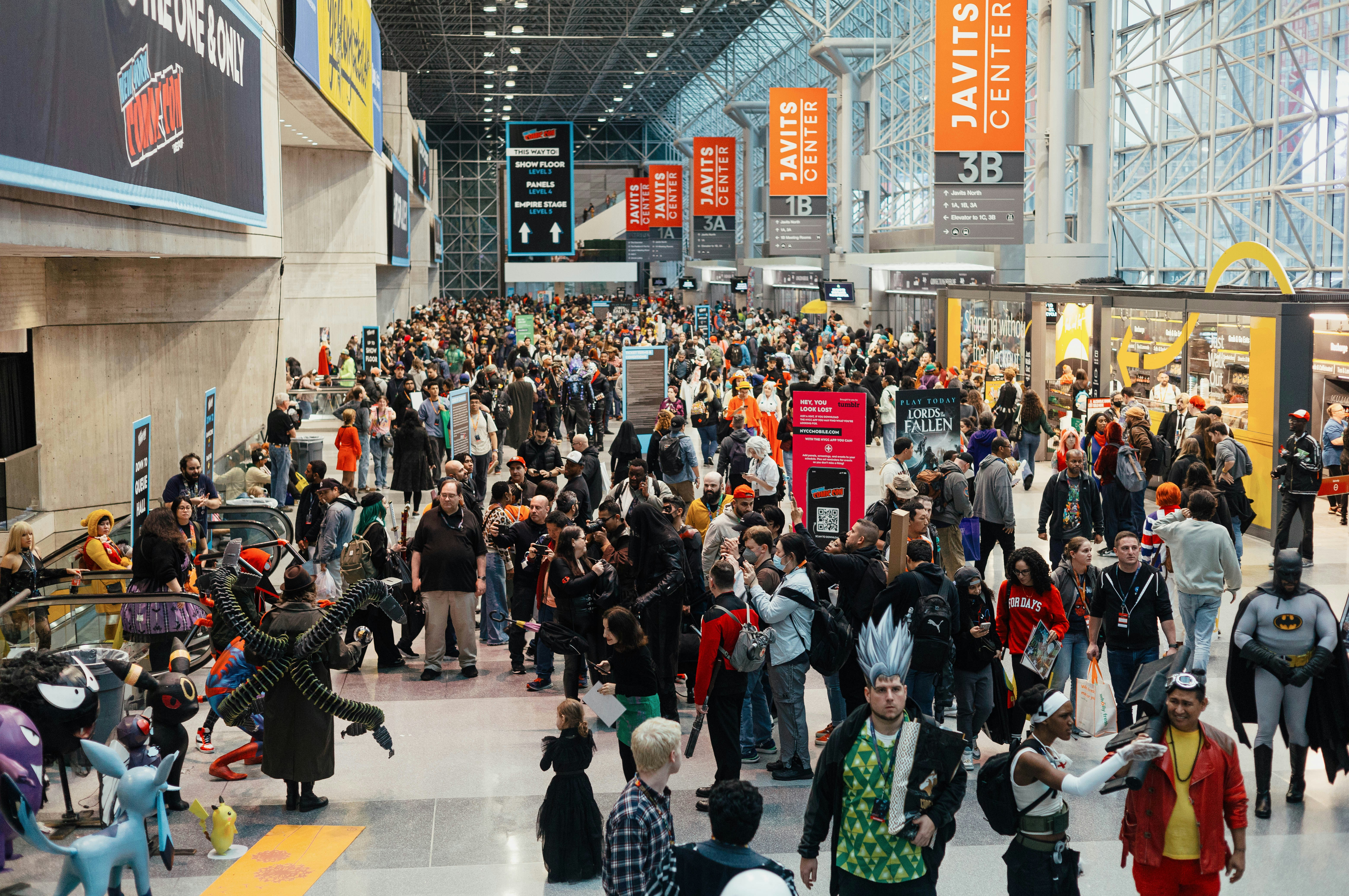 Large crowd at anime convention with attendees in cosplay costumes inside a busy convention center hallway 