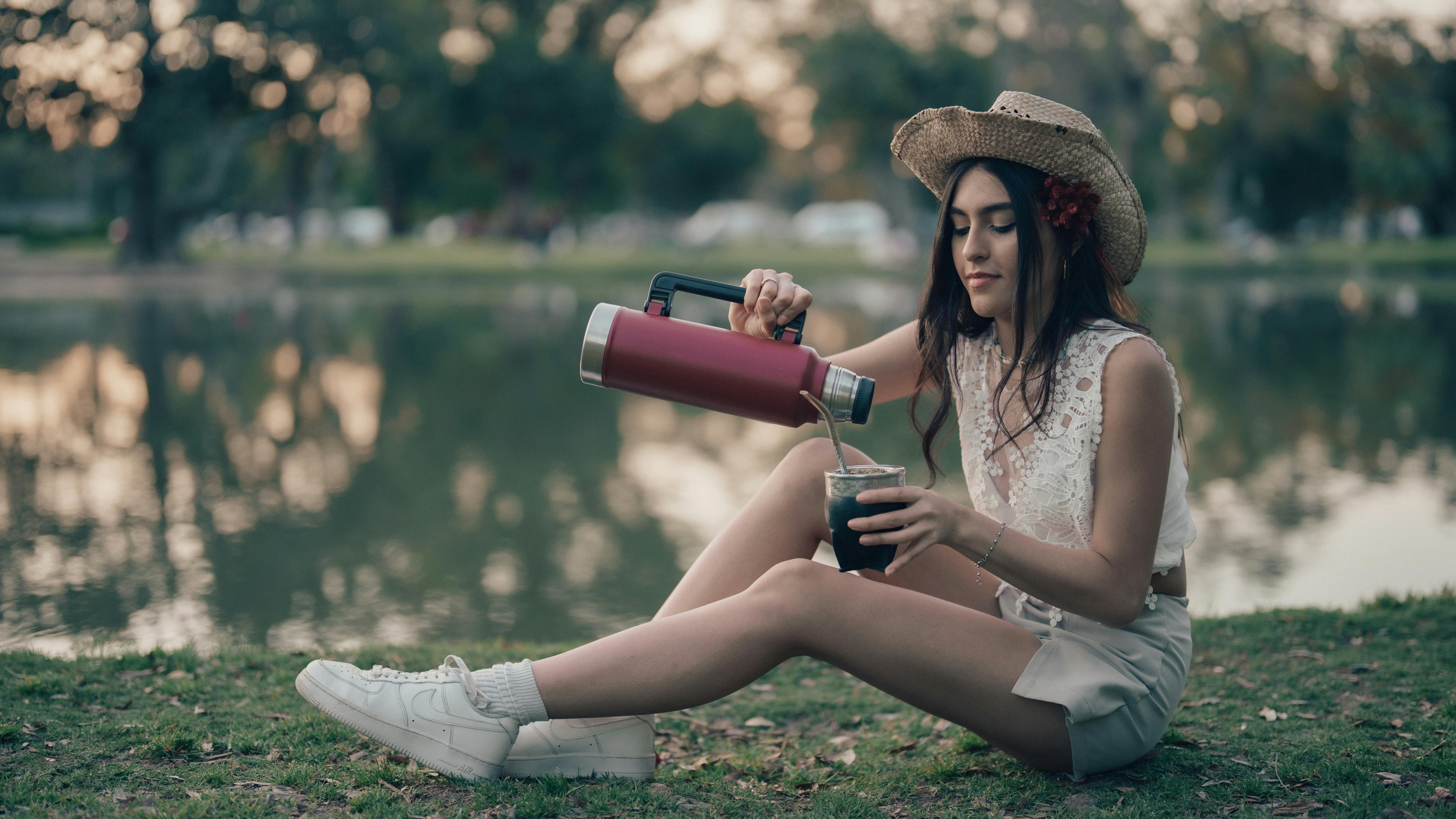 Woman pouring a drink from a reusable bottle near a lake, representing recalled Thermos bottles and defective product injury risks.
