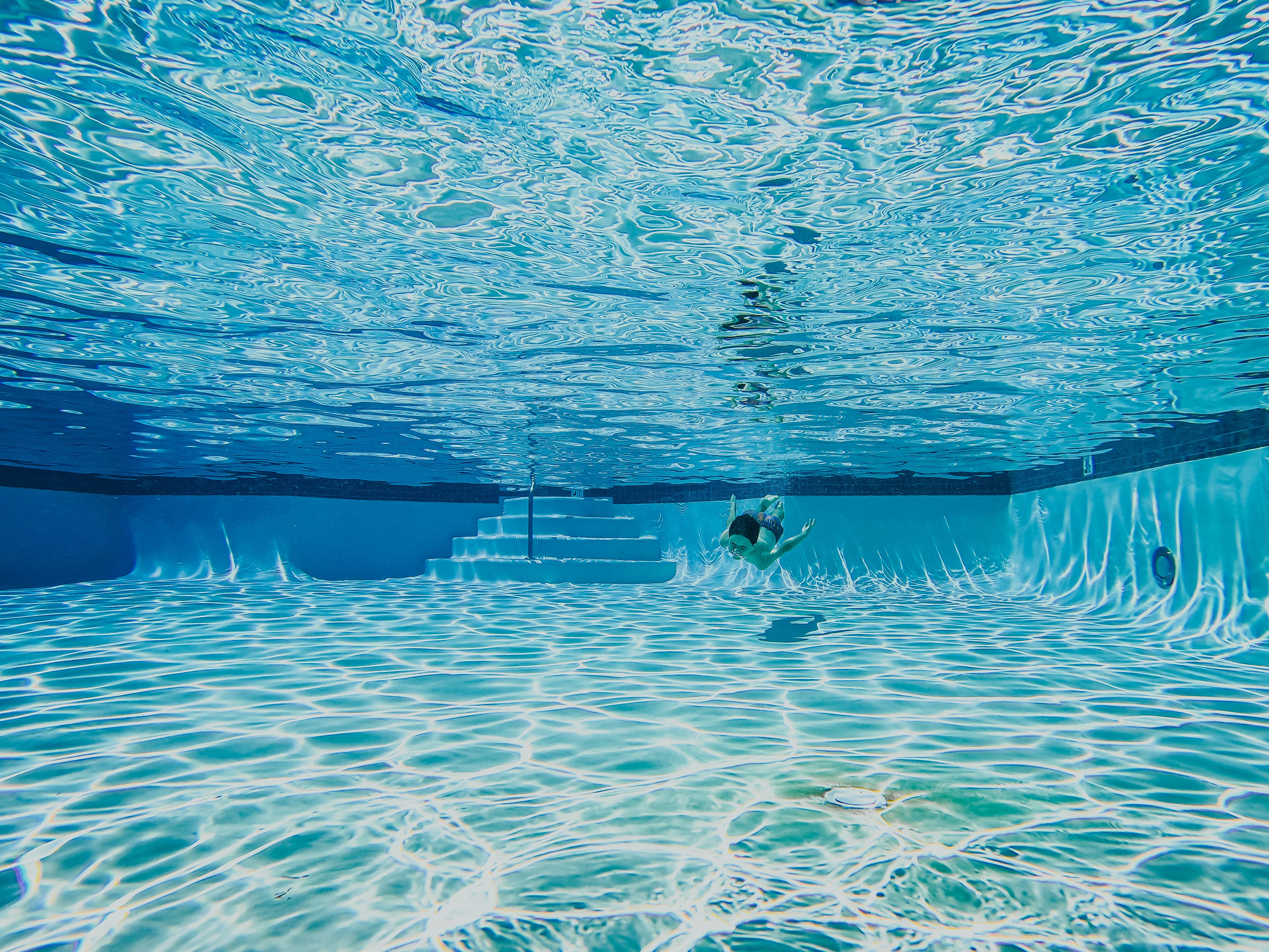 Underwater view of a swimmer in a clear blue pool with visible pool steps and lane dividers