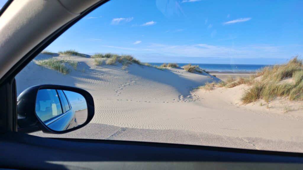 View from a car window of sand dunes and beach grass beside a road leading to the ocean at the Jersey Shore.