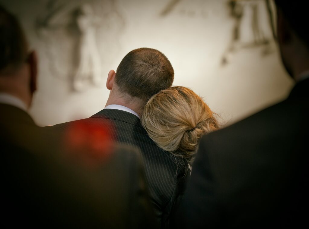 Grieving woman resting her head on a man's shoulder at a memorial service, a moment many families face before continuing a lawsuit after death.