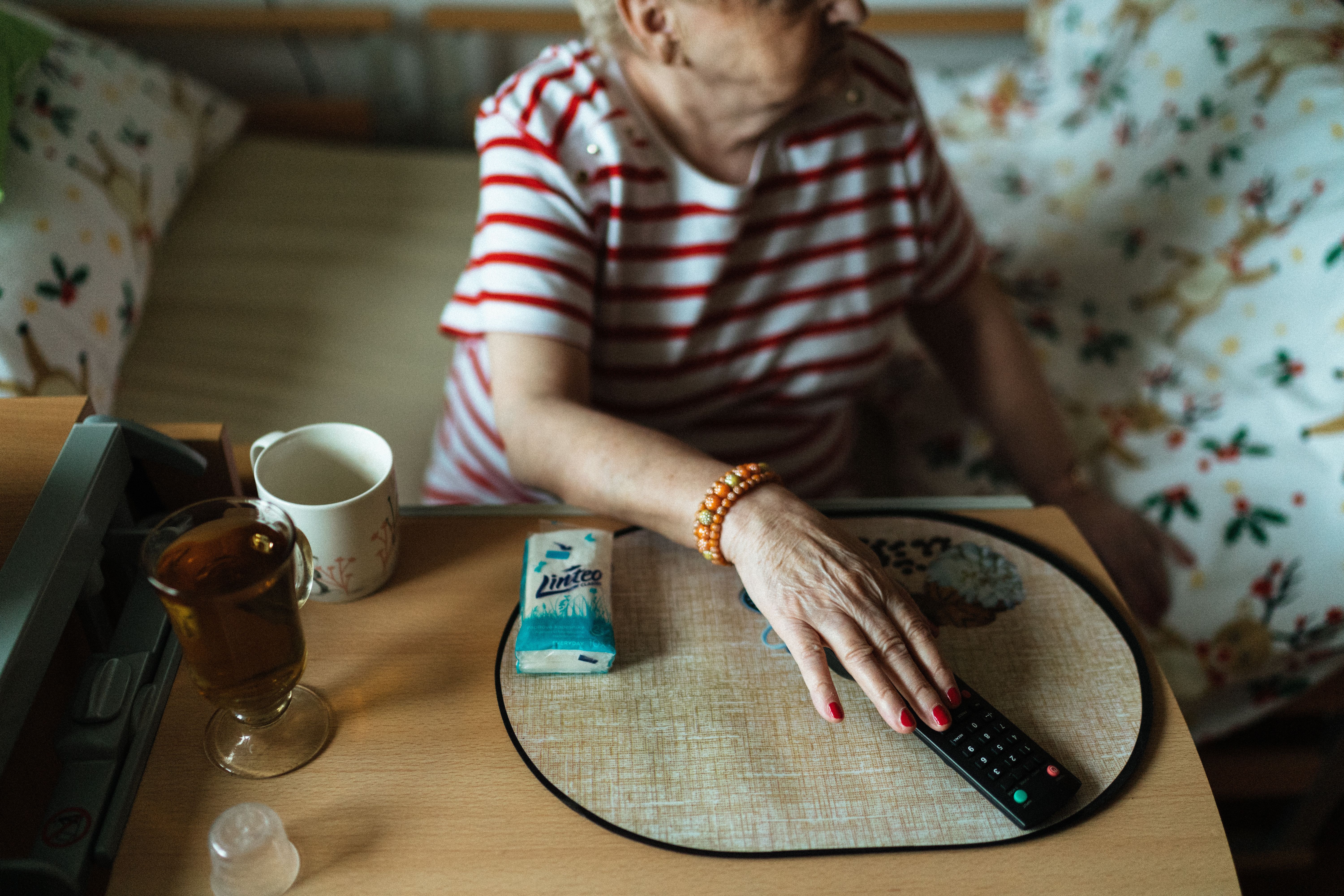 Elderly woman at a bedside table with tea and a TV remote, a quiet reminder of the risk of nursing home falls. 